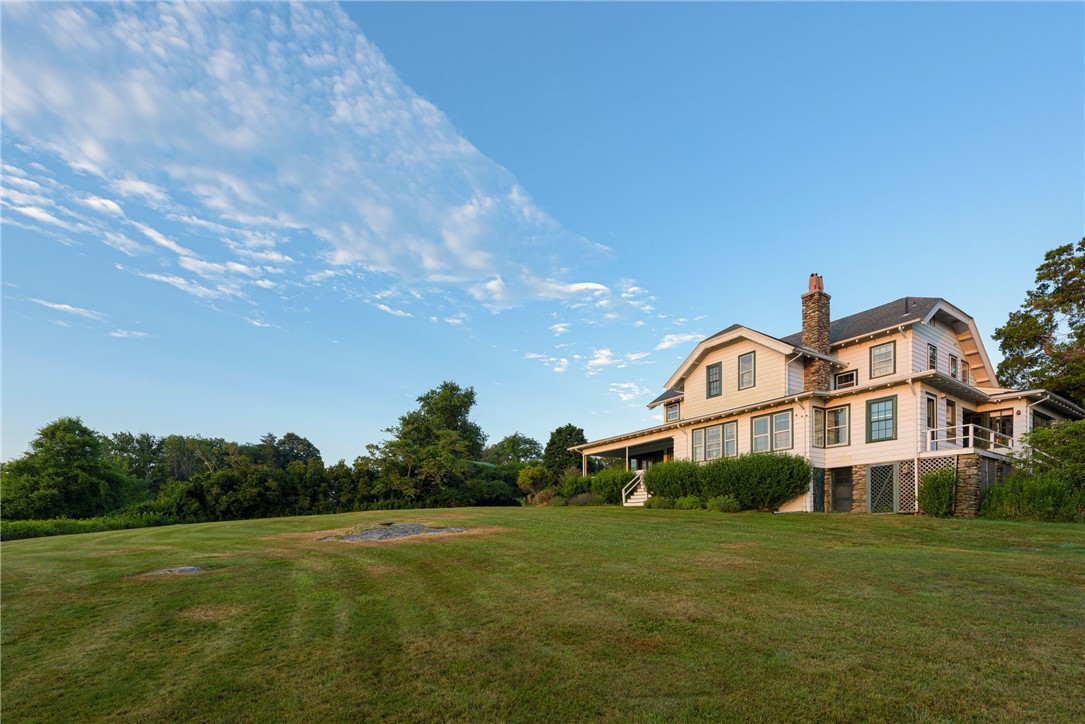 Large light-colored house with a stone chimney beside an expansive lawn.