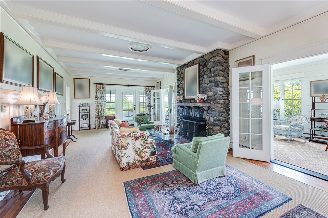 Living room with a stone fireplace, coffered ceiling, and French doors opening to a bright sunroom.