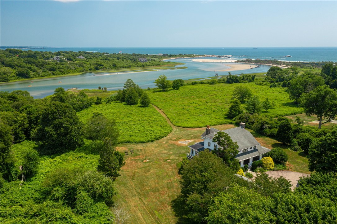 Aerial view of a coastal house beside green fields, an inlet, sandy beaches, and the ocean.