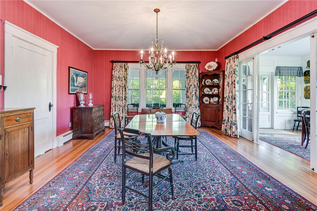 Dining room with coral-red walls, a long table, crystal chandelier, floral curtains, and patterned rug.