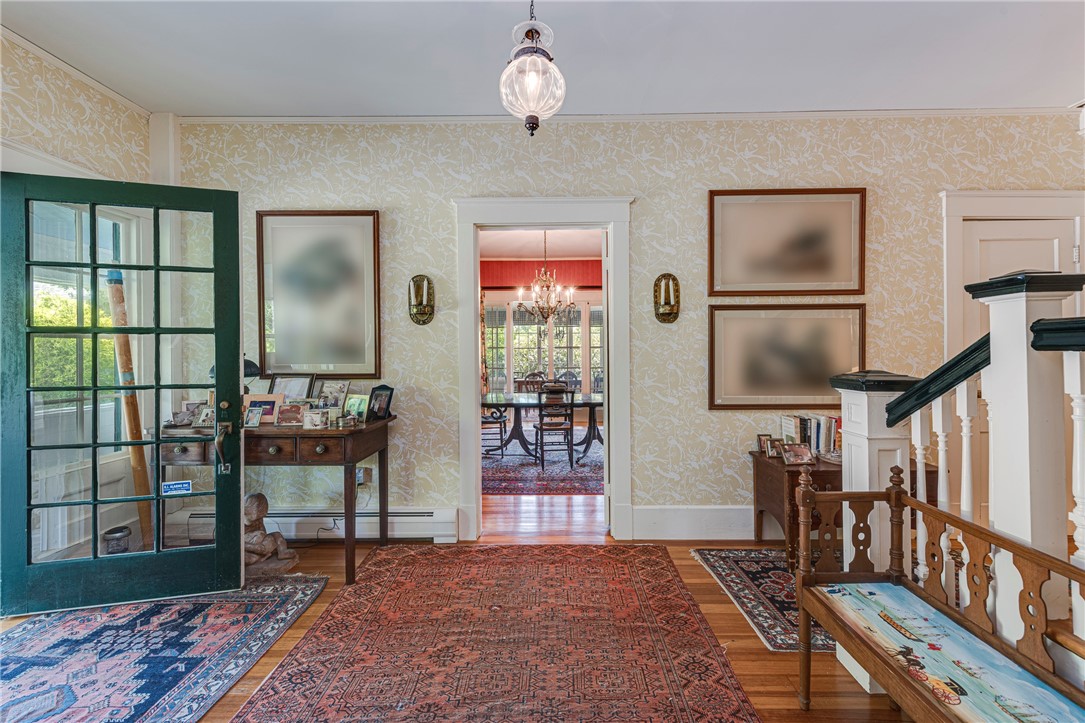 Furnished entry hall with patterned wallpaper, layered rugs, and a staircase with dark railings.