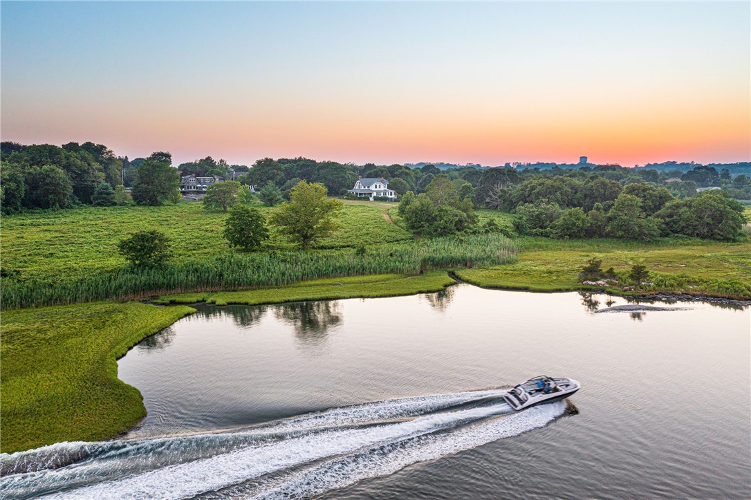 Aerial view of a coastal marsh and inlet at sunset, with a motorboat crossing the water.
