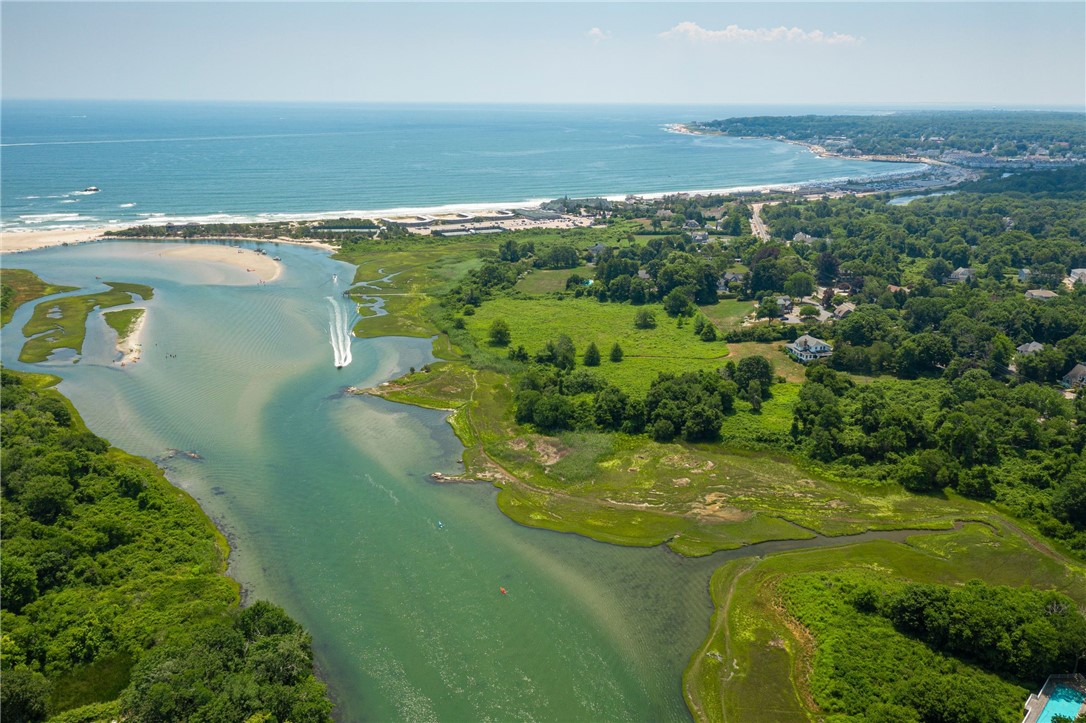 Aerial coastal view of an ocean beach, tidal inlet, green marshland, and scattered homes.