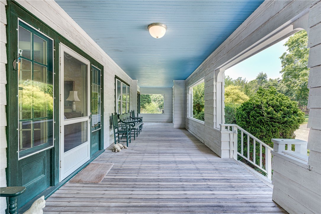 Covered porch with a blue ceiling, green doors, wooden chairs, and leafy garden views.