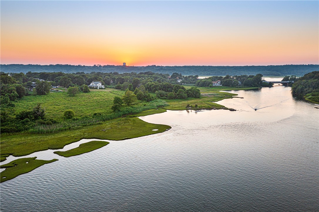 Aerial view of a tidal inlet and marsh at sunset, with homes along the wooded shore.