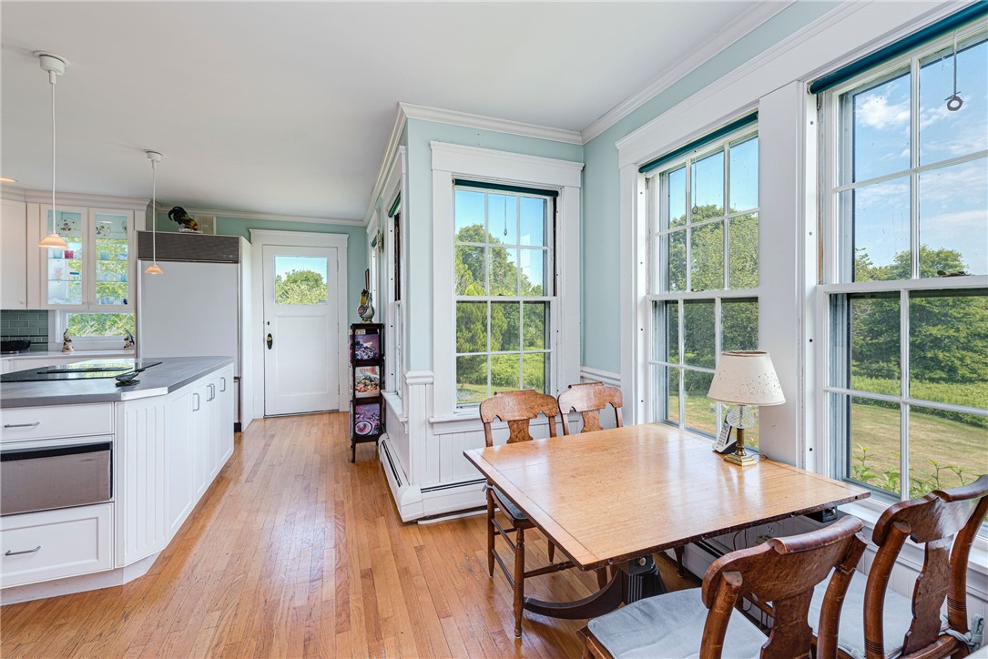 Dining area with a wooden table beside tall windows overlooking a lawn and trees.