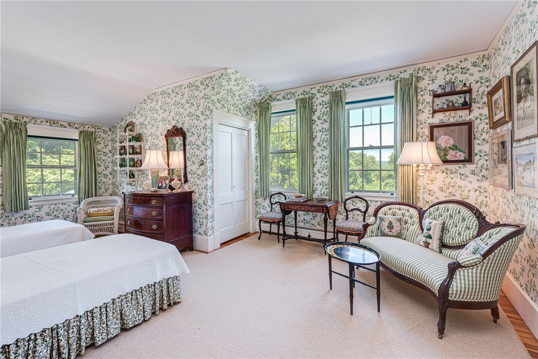 Bedroom with floral wallpaper, two beds, and a striped settee beside tall windows.