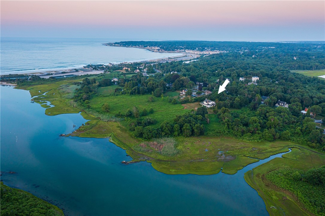 Aerial view of a coastal home beside salt marshes, marked by a white arrow.