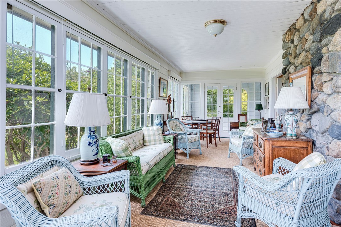 Bright sunroom with wicker seating, tall windows, a green settee, and a stone wall.