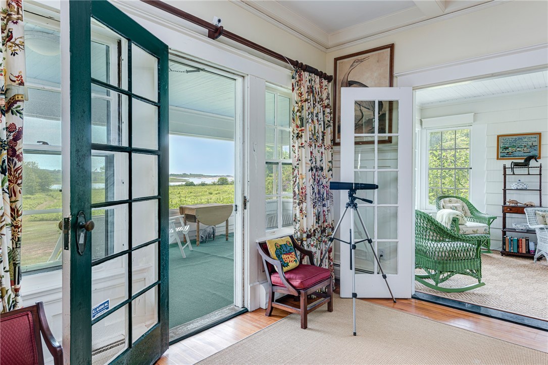 Sunroom with French doors, a telescope, wicker seating, and views across marshland to the water.