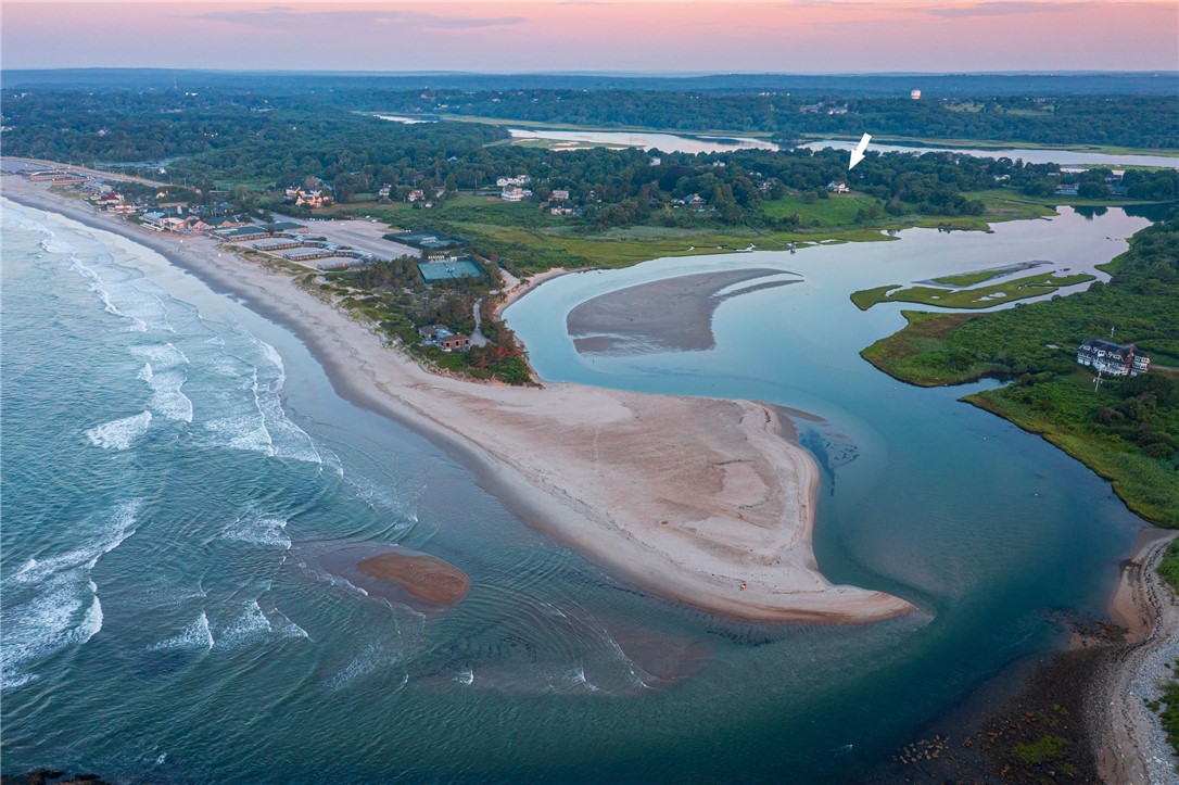 Aerial coastal view with a white arrow marking the property beside a sandy beach and tidal inlet.