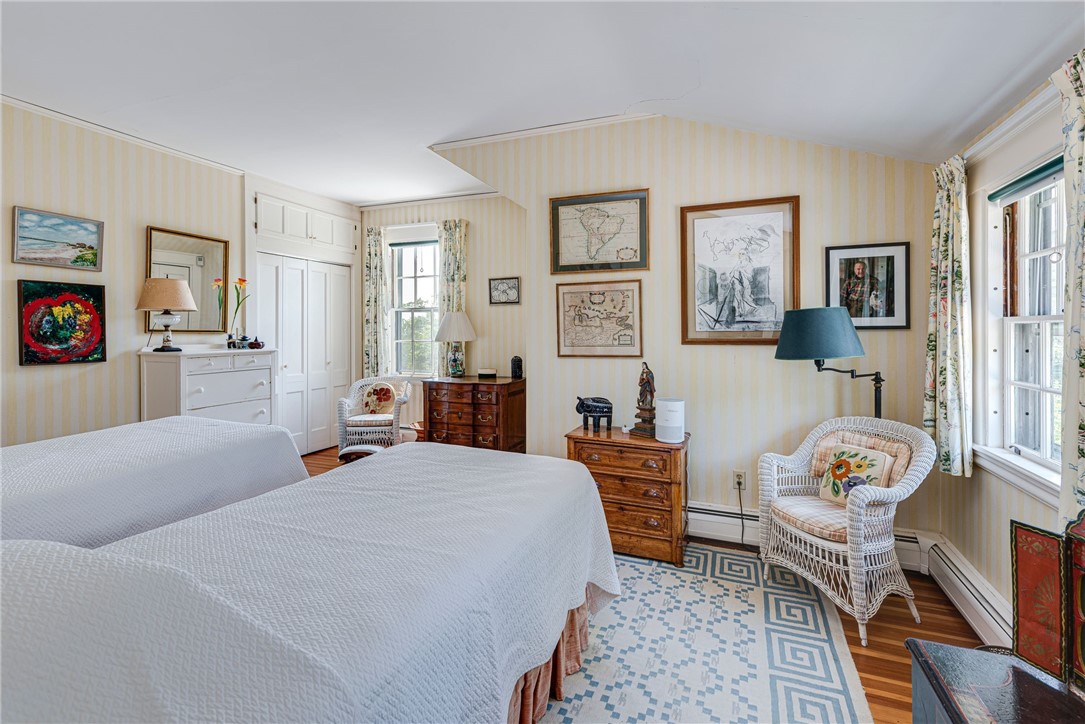 Bedroom with two white-covered beds, striped wallpaper, wicker chairs, and a blue geometric rug.