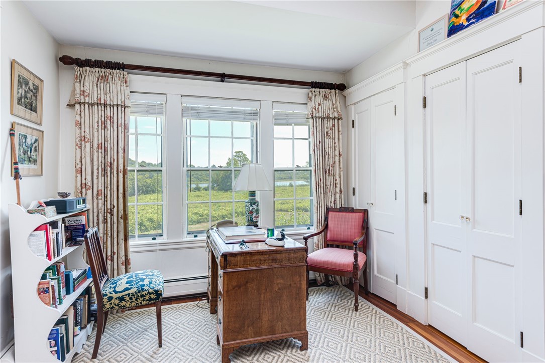Home office with a wooden desk, patterned chairs, and large windows overlooking marshland and water.