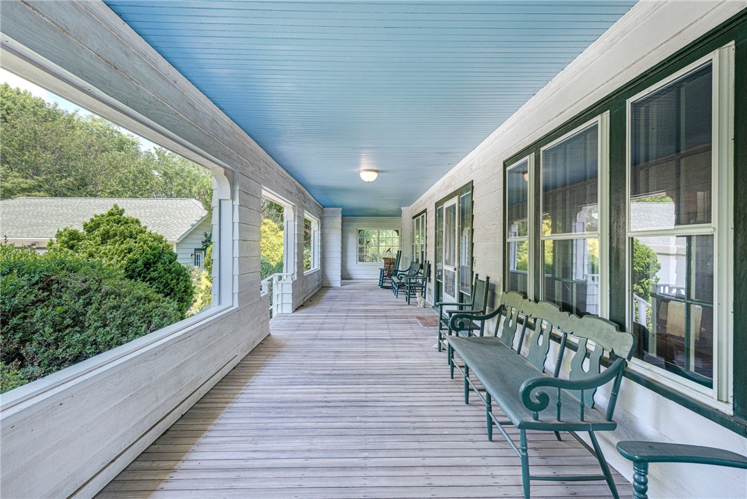 Covered porch with a pale blue ceiling, white plank floor, and green benches beside large windows.