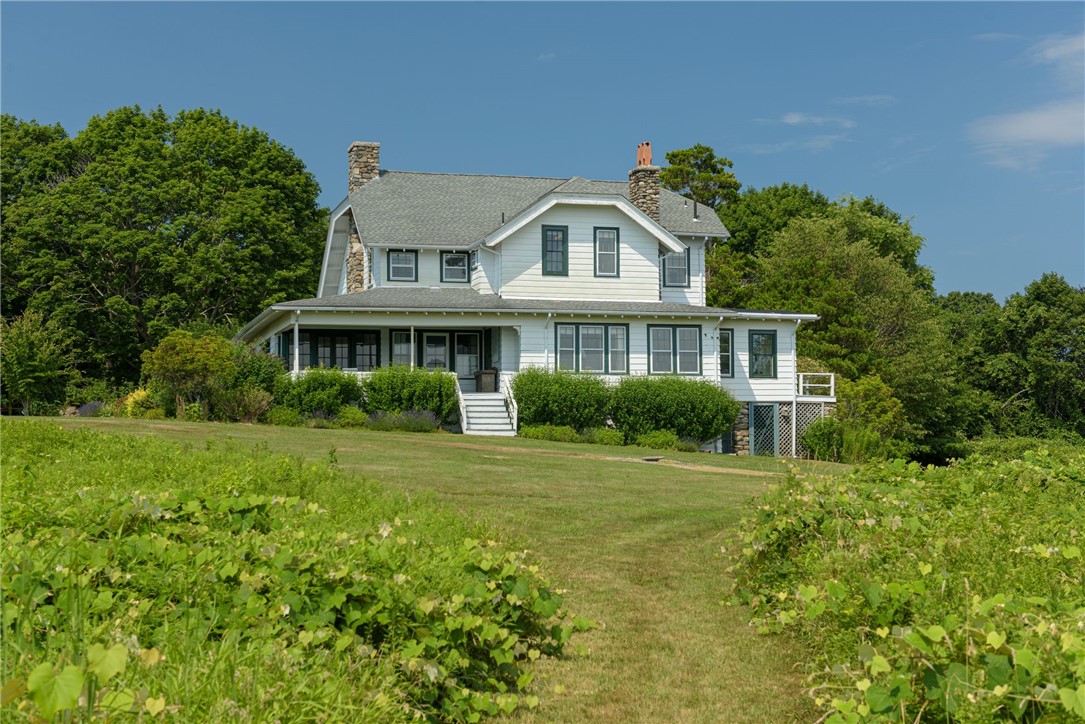 White two-story home with stone chimneys and a covered porch, set behind a broad lawn.