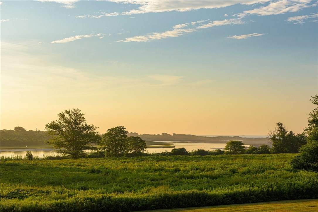 Coastal marsh and water at golden hour, with a distant shoreline beneath a cloud-streaked sky.