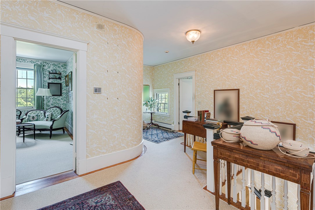 Furnished hall with floral wallpaper, wooden console tables, and a doorway to a sitting room.