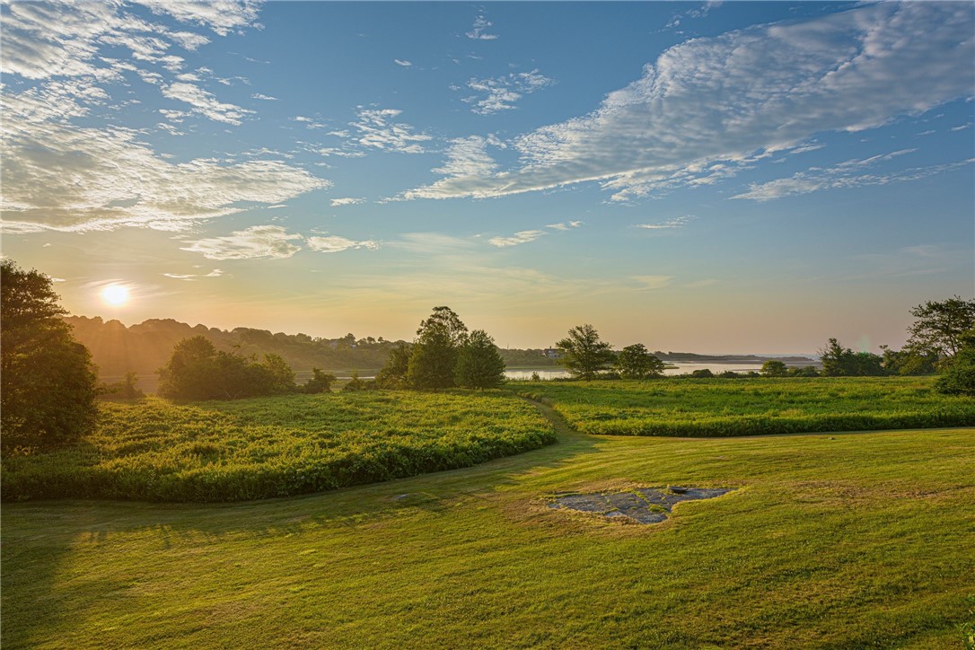 Lawn and marshland meet a distant water view beneath a cloud-streaked sunset sky.