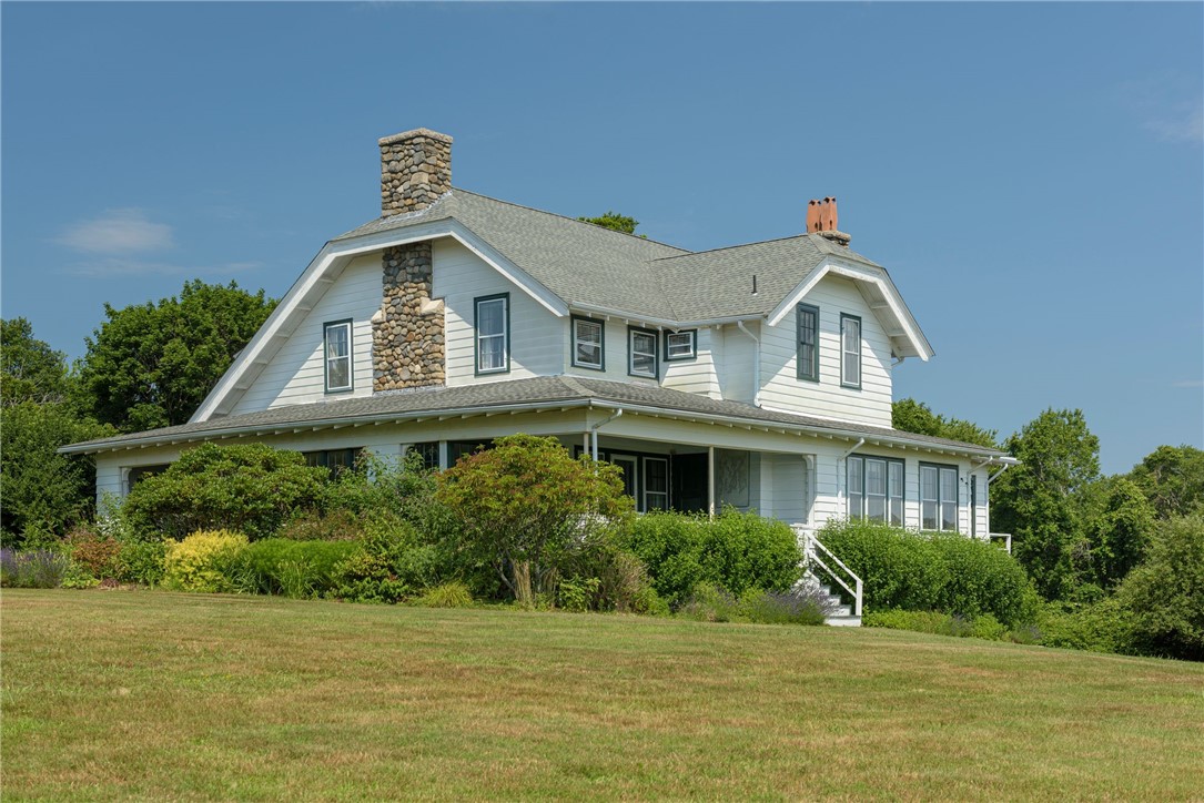 White two-story house with a stone chimney and wraparound porch, set behind a broad lawn.
