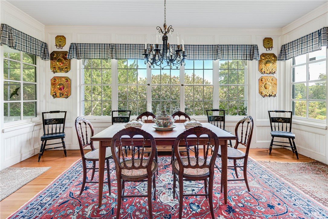 Dining room with antique chairs, a patterned rug, chandelier, and large windows overlooking greenery.