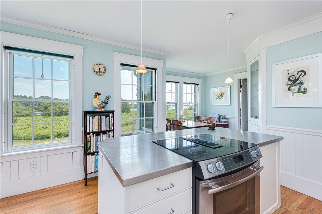 Bright kitchen with a large island and stainless steel range, overlooking green fields through multiple windows.