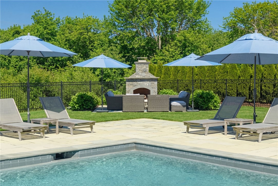 Outdoor pool with blue umbrellas, lounge chairs, and a stone fireplace seating area.