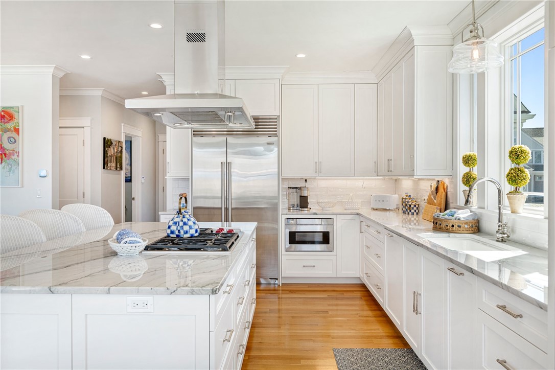 Bright white kitchen with a marble island, gas cooktop, stainless steel appliances, and warm wood floors.