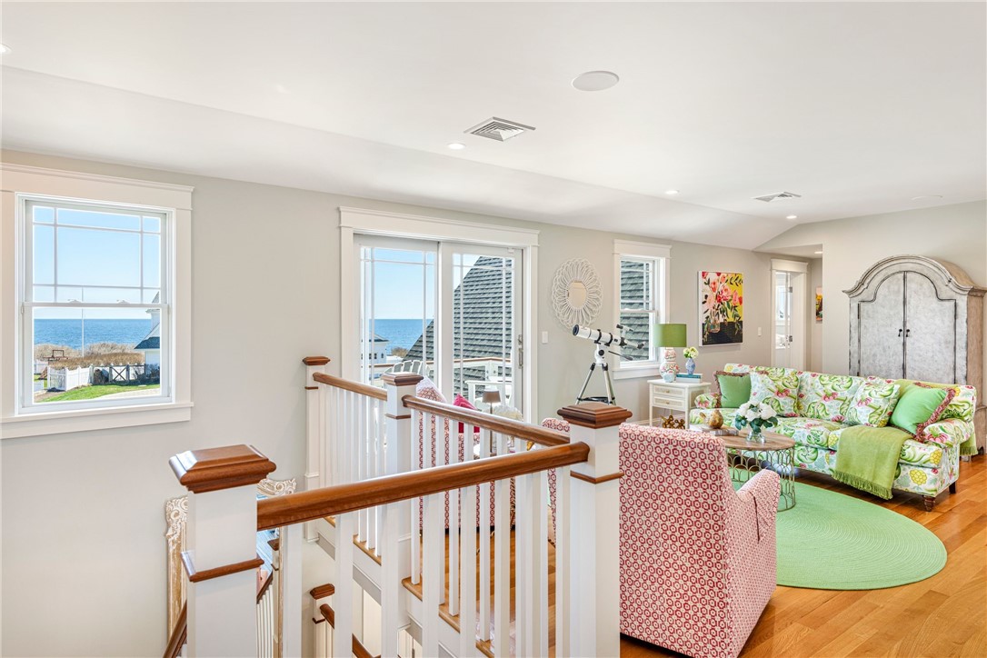 Ocean-view living room with floral seating, green rug, telescope, and open staircase.