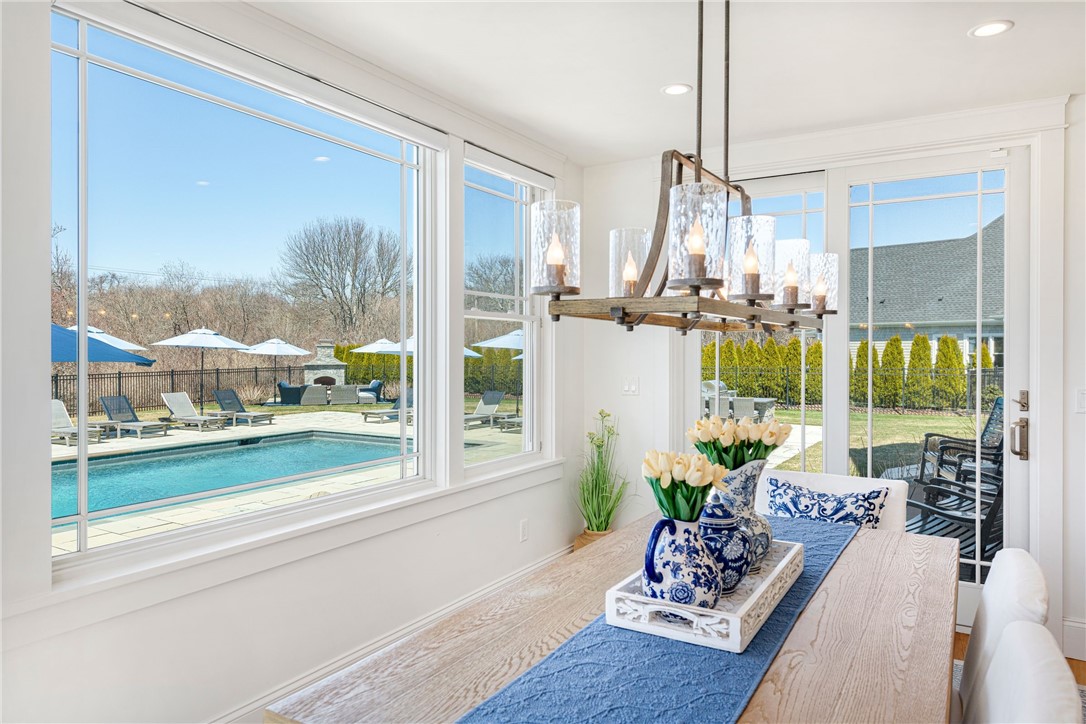 Dining area with a wood table and chandelier overlooking a backyard pool through large windows.