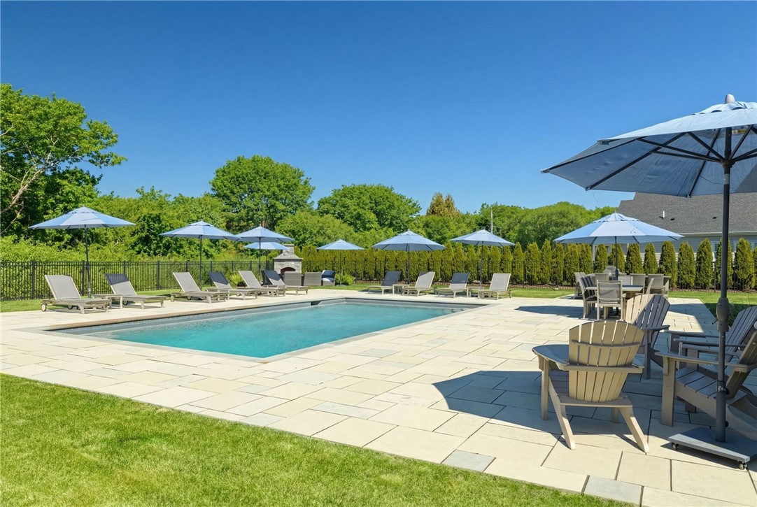 Outdoor swimming pool surrounded by a stone patio, lounge chairs, and umbrellas.
