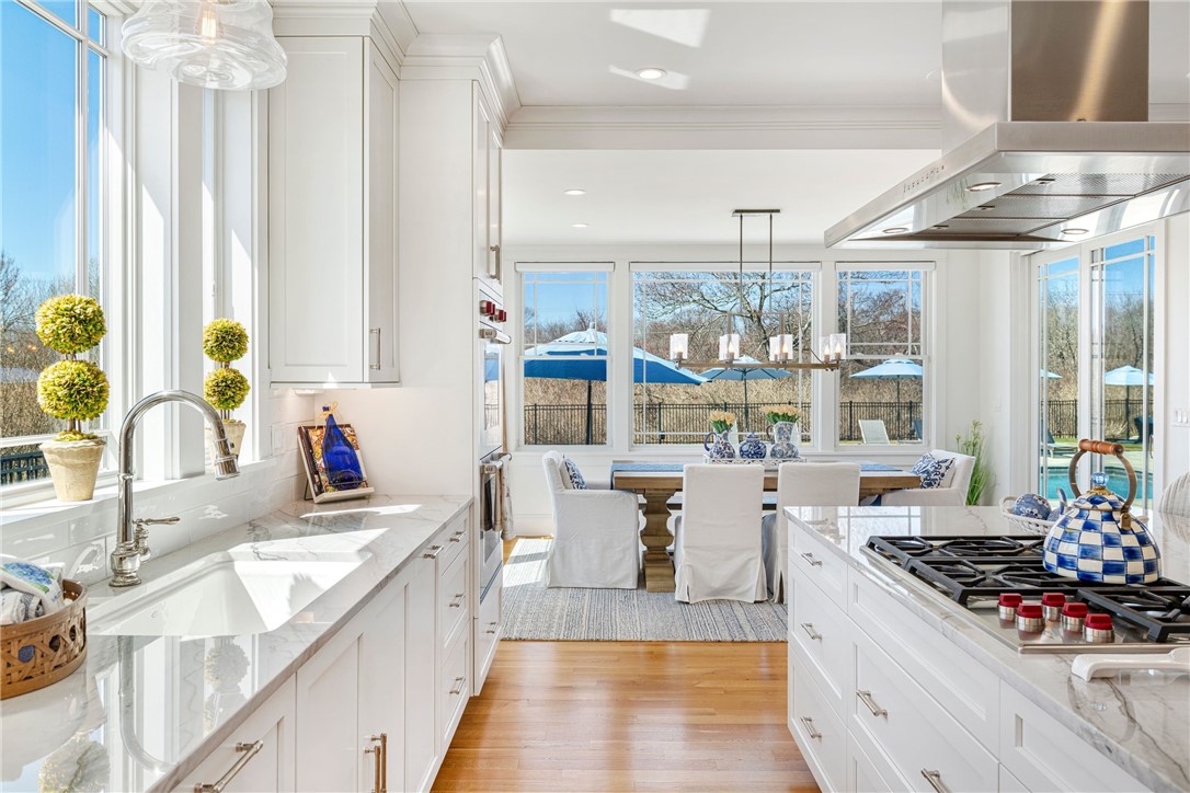 Bright white kitchen with marble counters, a farmhouse sink, and windows overlooking a fenced pool.