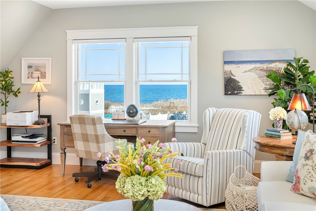 Sitting room with striped armchairs and a desk facing large ocean-view windows.