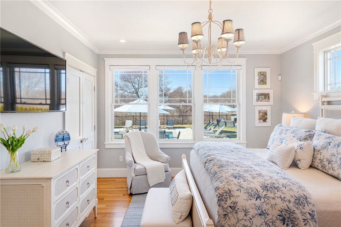 Furnished bedroom with blue floral bedding, a chandelier, and tall windows overlooking a pool patio.