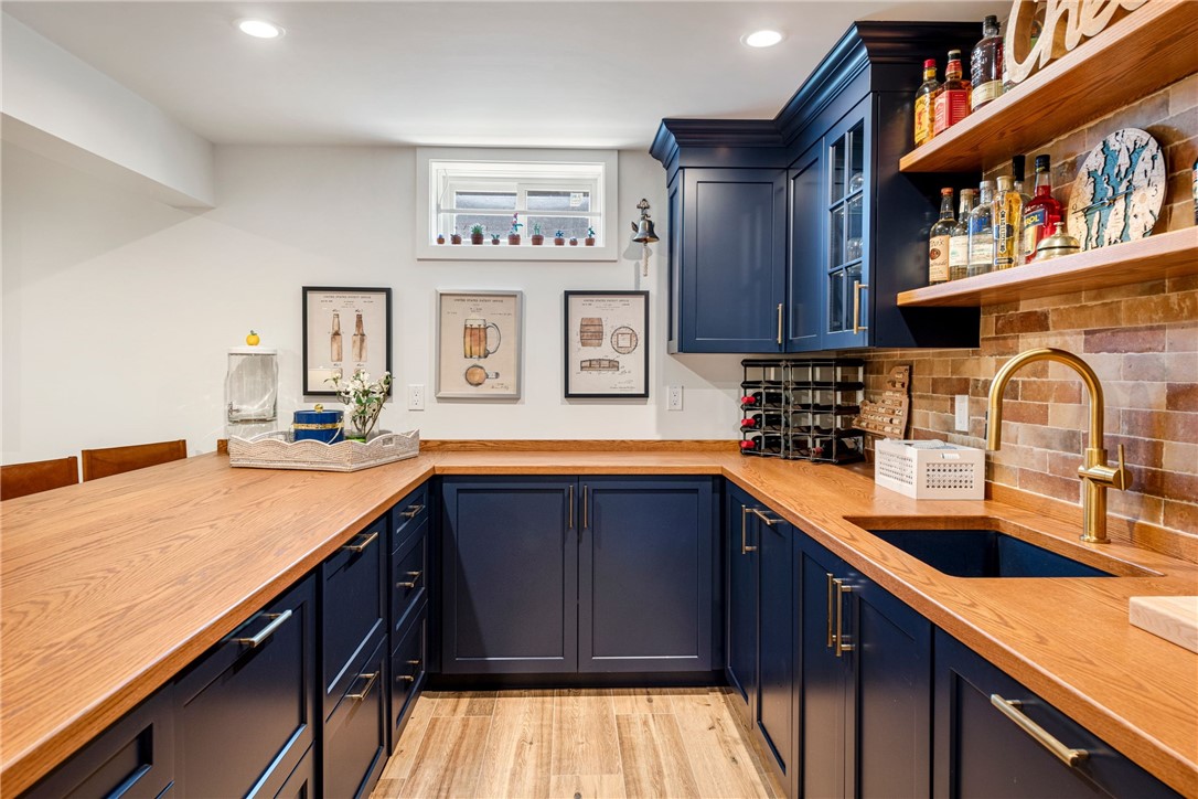 Kitchen with navy cabinetry, oak counters, brick backsplash, and brass fixtures.