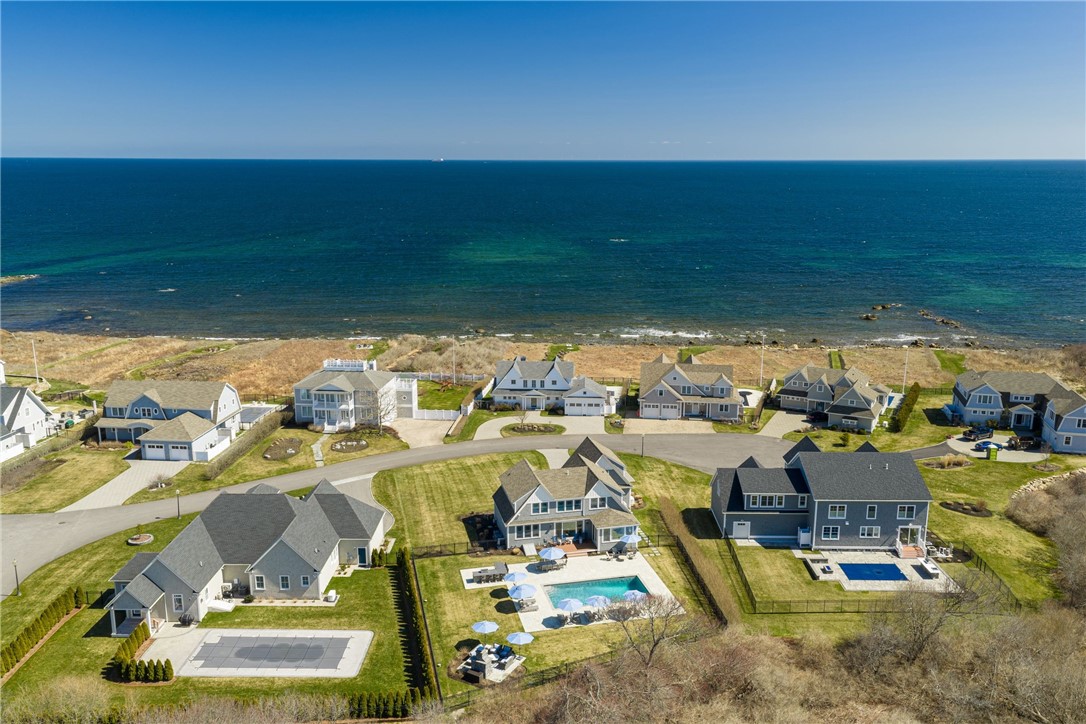 Coastal homes and backyard pools beside the ocean, seen from above.
