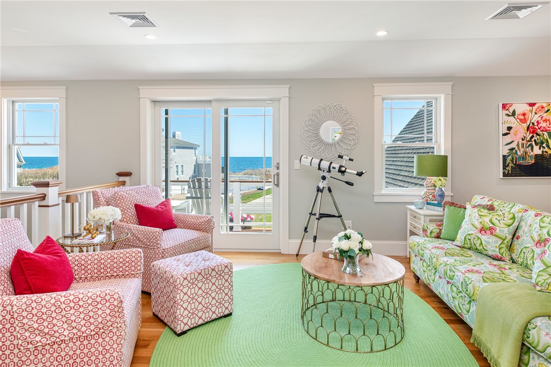 Living room with a telescope beside ocean-facing glass doors and colorful patterned seating.