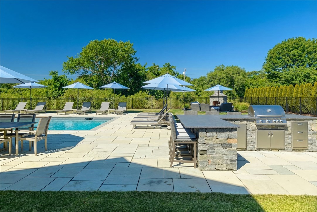 Outdoor pool patio with blue umbrellas, lounge chairs, and a stone outdoor kitchen.