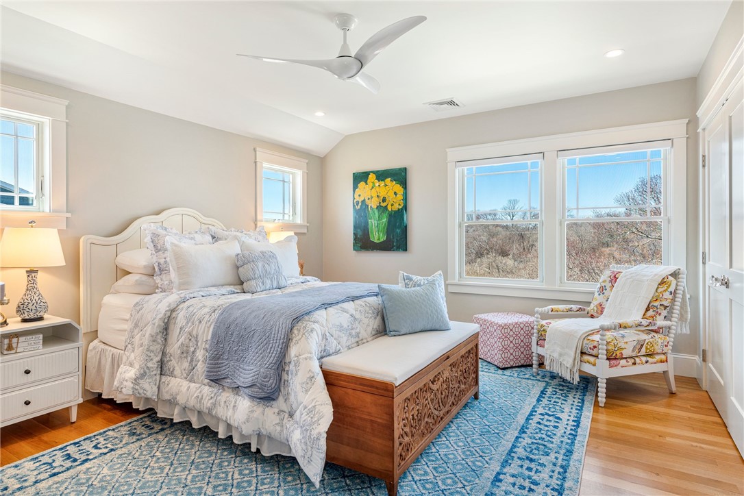 Bedroom with blue-and-white bedding, a patterned rug, and a floral armchair beside wide windows.