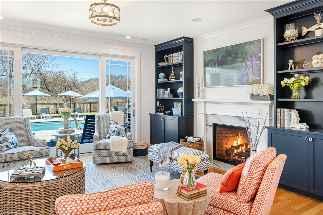 Living room with a white fireplace, navy built-ins, orange chairs, and sliding doors overlooking a pool.