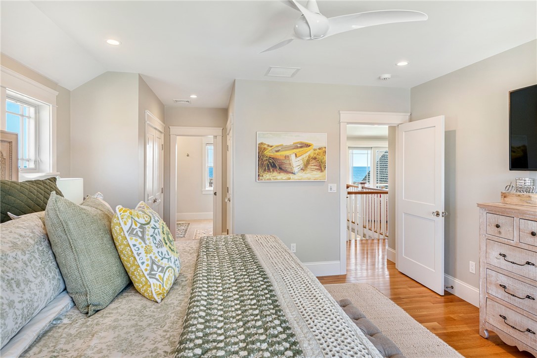 Bedroom with layered green bedding, hardwood floors, and a glimpse of the ocean through an open doorway.