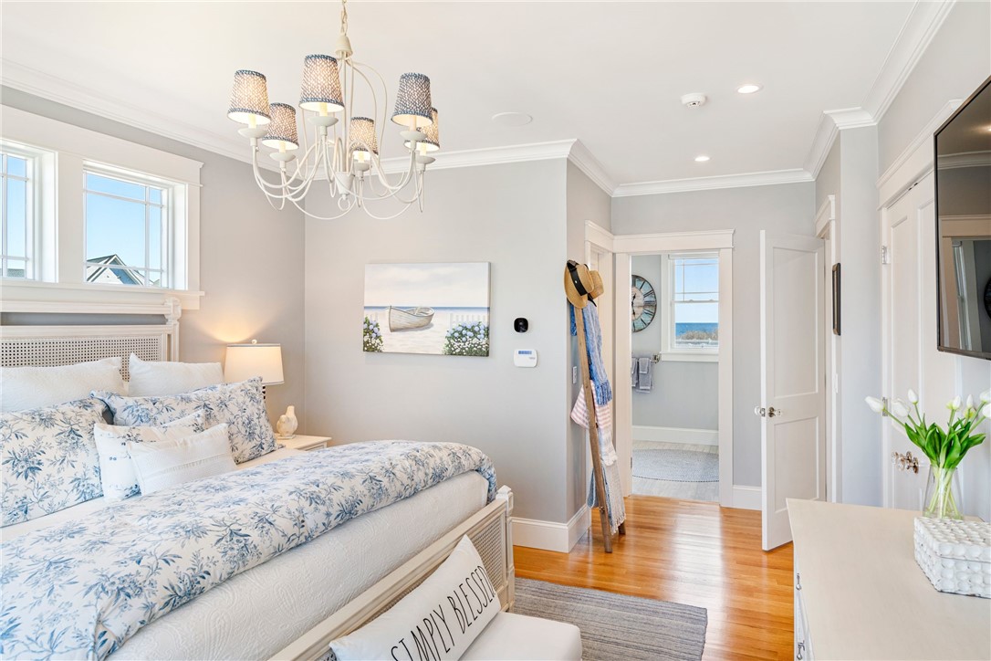 Bedroom with blue floral bedding, a chandelier, hardwood floors, and a water view through the doorway.