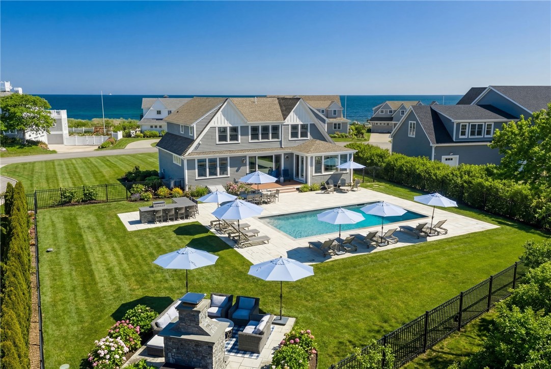 Coastal home with a swimming pool and patio, with the ocean visible beyond neighboring houses.