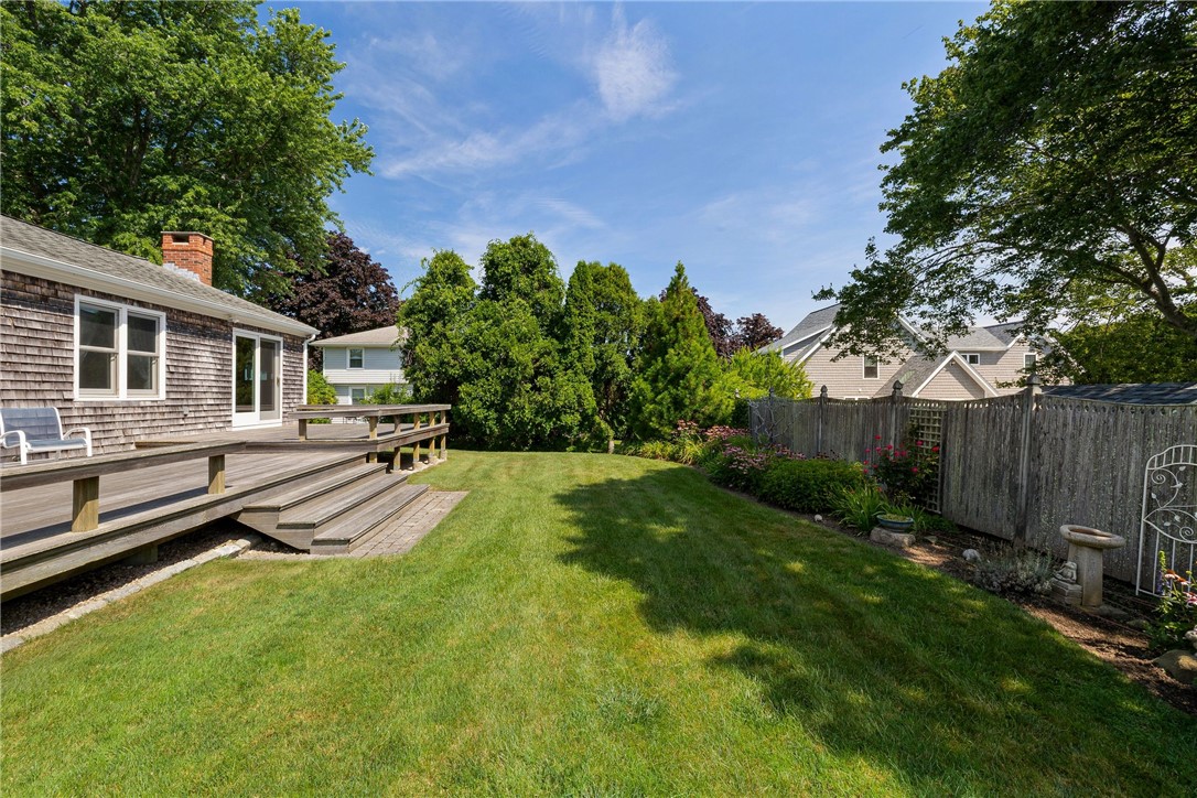Backyard with a broad lawn, raised wooden deck, mature trees, and wooden fence.