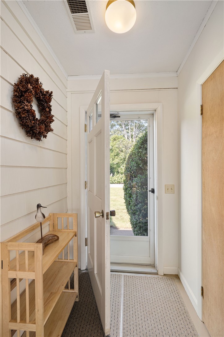 Entry hall with white shiplap walls, a wooden bench, and an open door to a leafy yard.
