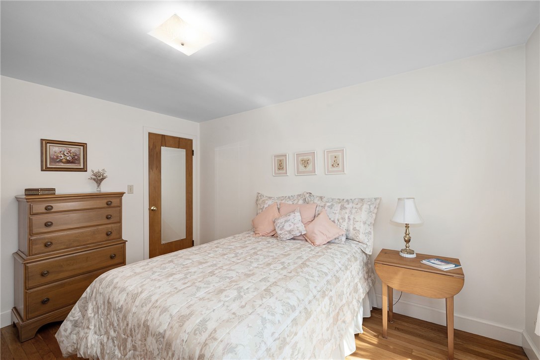 Bedroom with pale floral bedding, wooden dresser, and sunlight on the hardwood floor.