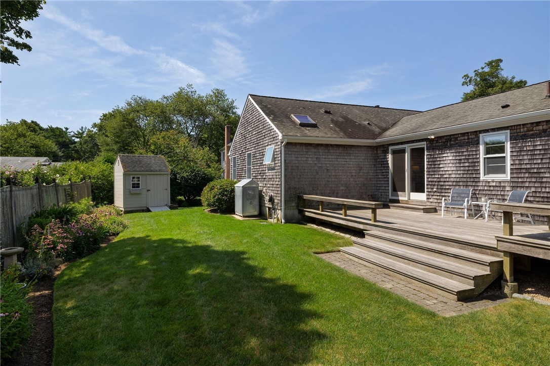 Cedar-shingle house with a raised deck, broad lawn, garden beds, and a small shed.