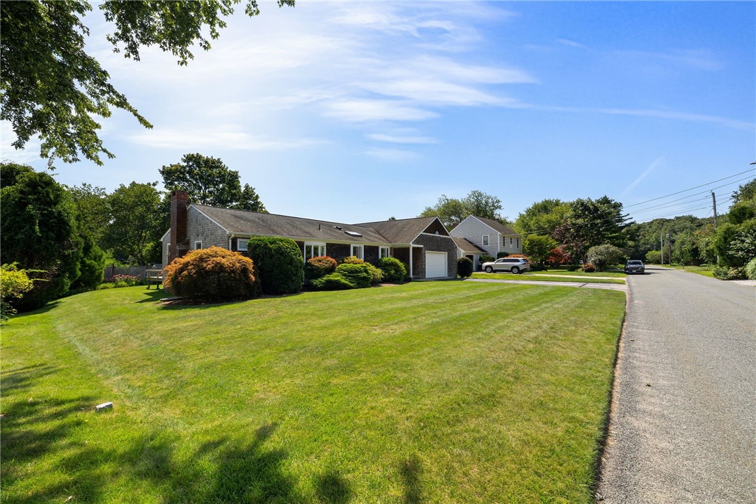 Single-story home with an attached garage, landscaped lawn, and mature trees beside a residential road.