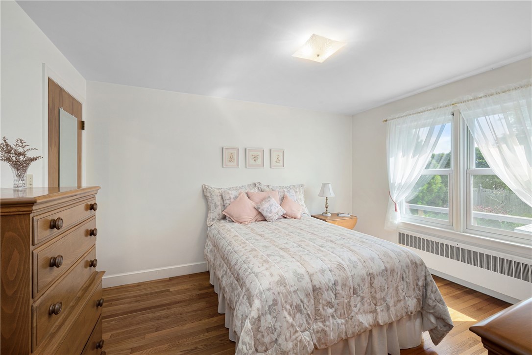 Bedroom with a floral-covered bed, wooden dresser, and large curtained windows.