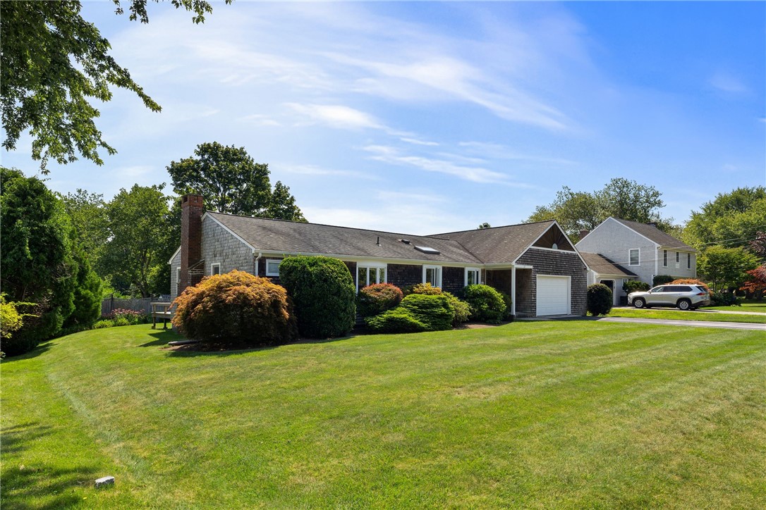 Single-story shingle home with a brick chimney, attached garage, and broad green lawn.