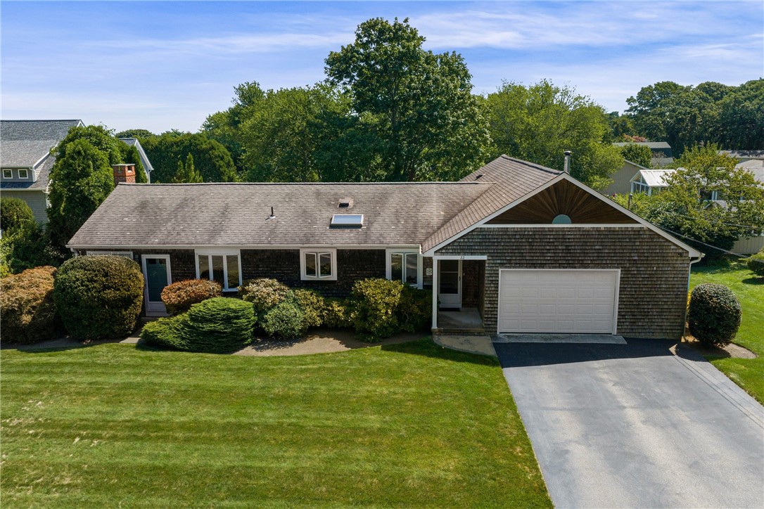 Single-story shingle-sided home with a prominent gabled entry, attached garage, landscaped shrubs, and broad lawn.